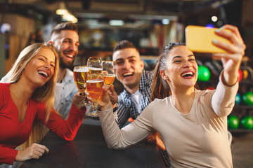 Компания друзей пьет пиво и фотографируется в баре