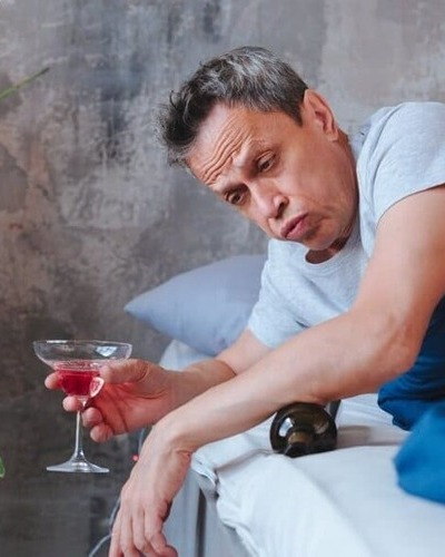 Мужчина с бокалом алкоголя сидит в кровати