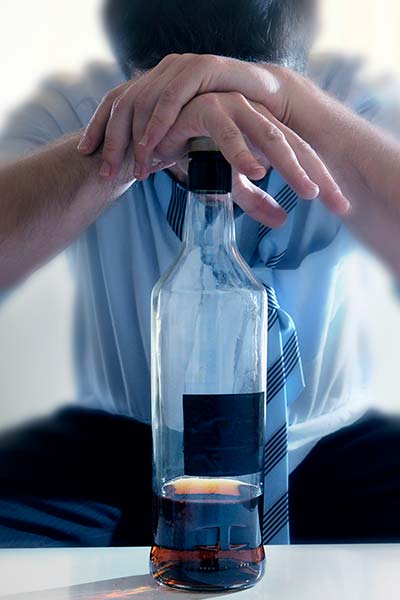 грустный мужчина сидит на диване, опираясь на бутылку с алкоголем