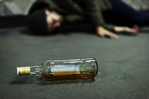 пьяный мужчина спит на полу рядом с бутылкой алкоголя